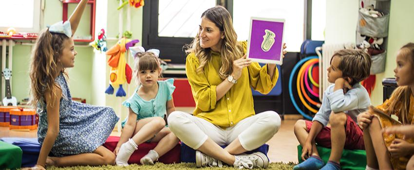 Teacher holding up book while kids sit on carpet in a circle.